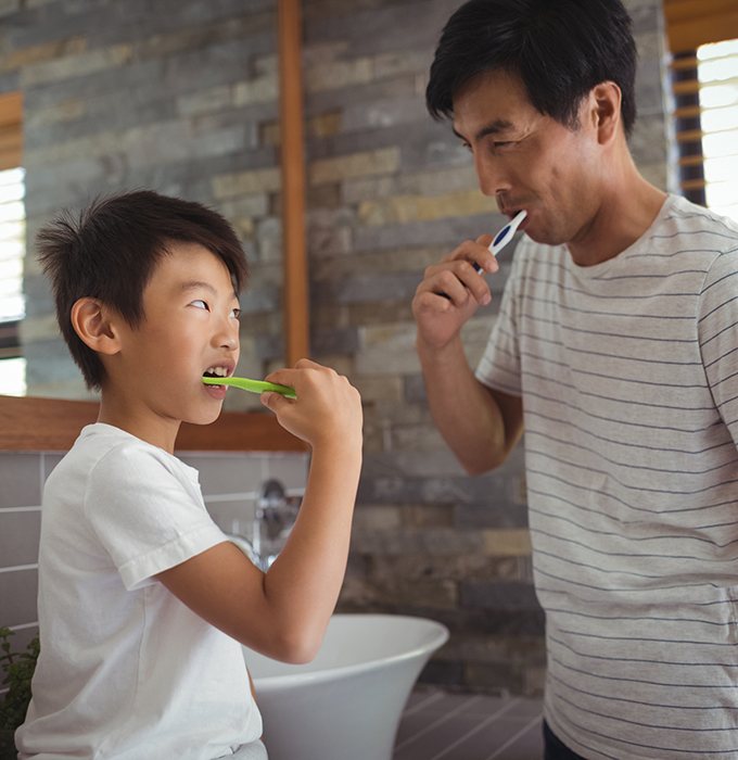 a father and child brushing their teeth together